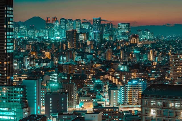 Illuminated city buildings at dusk beneath an orange sky